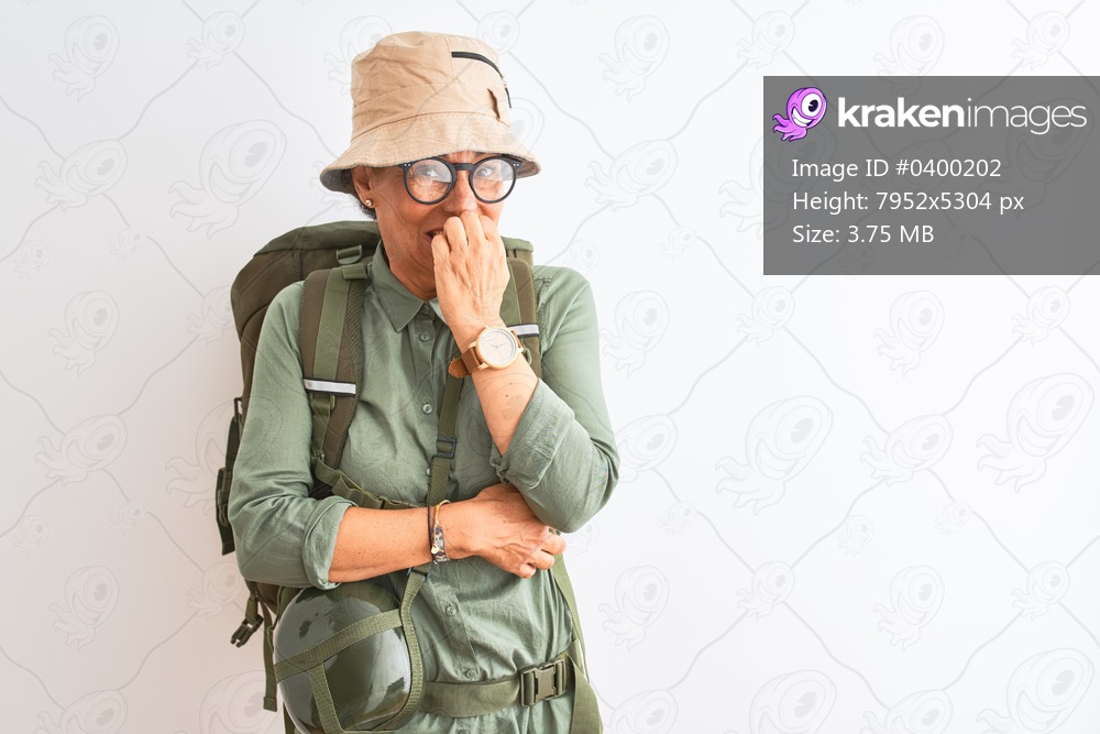 Middle age hiker woman wearing backpack canteen hat glasses over isolated white background looking stressed and nervous with hands on mouth biting nails. Anxiety problem.