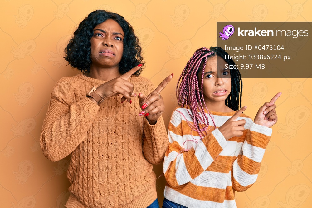 Beautiful african american mother and daughter wearing wool winter sweater pointing aside worried and nervous with both hands, concerned and surprised expression 