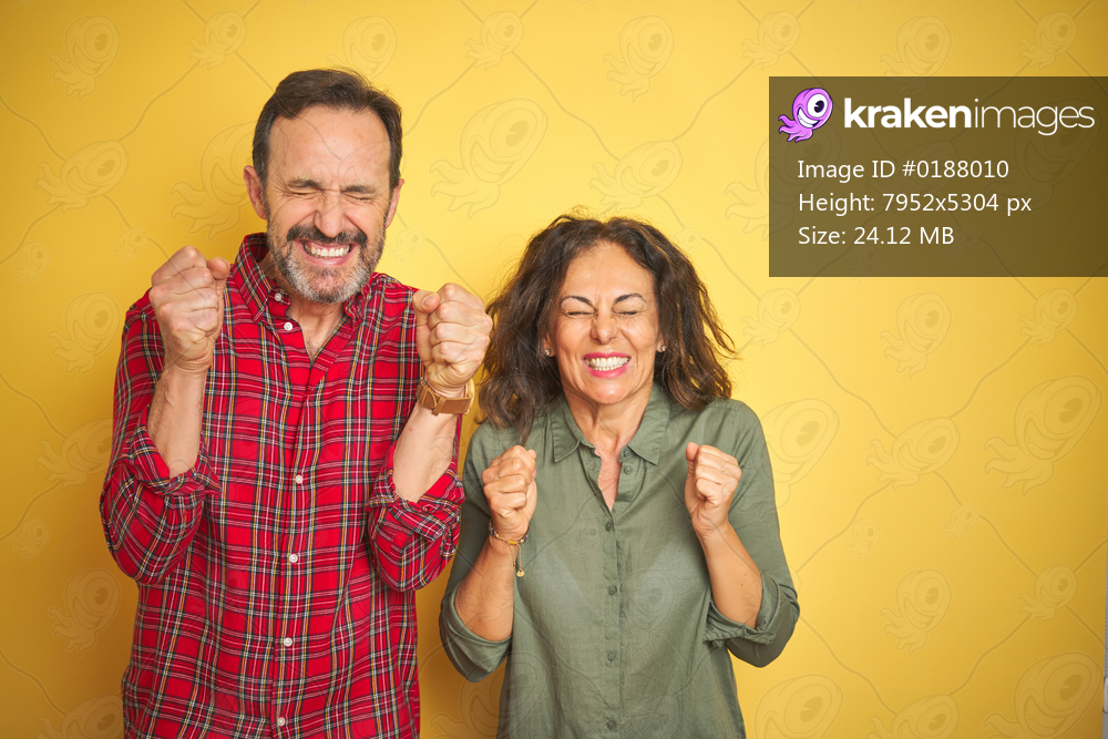 Beautiful middle age couple over isolated yellow background excited for success with arms raised and eyes closed celebrating victory smiling. Winner concept.