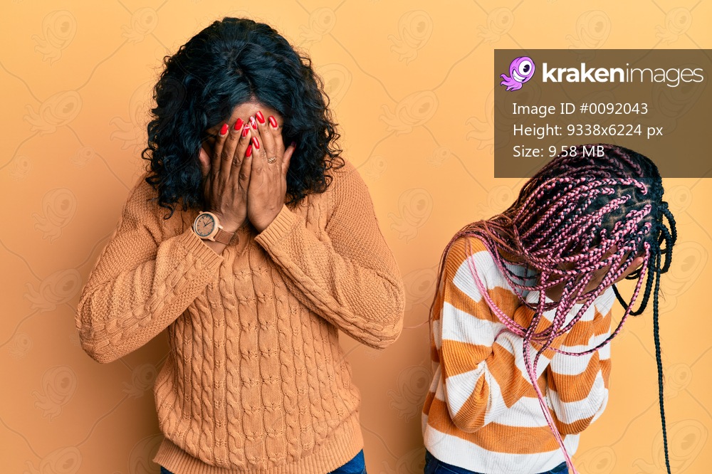 Beautiful african american mother and daughter wearing wool winter sweater with sad expression covering face with hands while crying. depression concept. 