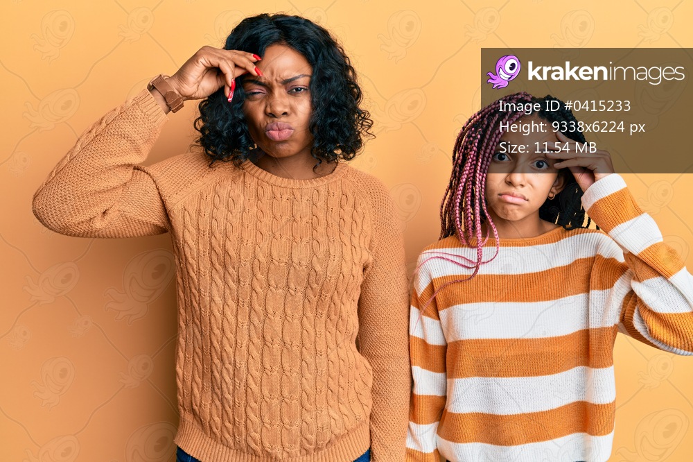 Beautiful african american mother and daughter wearing wool winter sweater worried and stressed about a problem with hand on forehead, nervous and anxious for crisis 