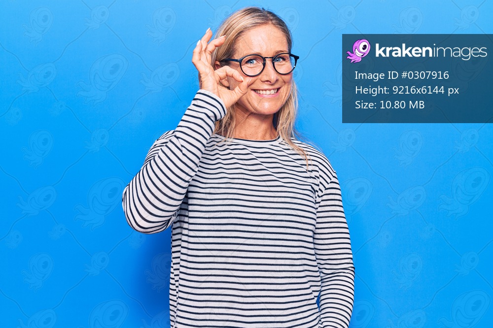 Middle age caucasian blonde woman wearing casual striped sweater and glasses smiling positive doing ok sign with hand and fingers. successful expression. 