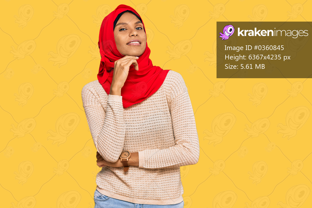 Young african american woman wearing traditional islamic hijab scarf looking confident at the camera smiling with crossed arms and hand raised on chin. thinking positive. 