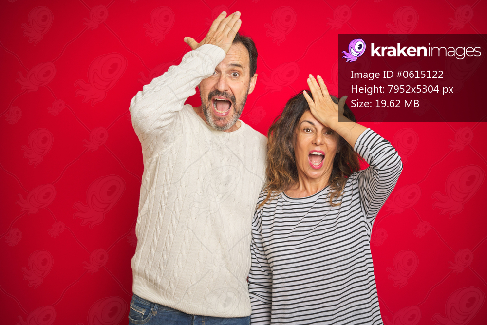 Beautiful middle age couple wearing winter sweater over isolated red background surprised with hand on head for mistake, remember error. Forgot, bad memory concept.