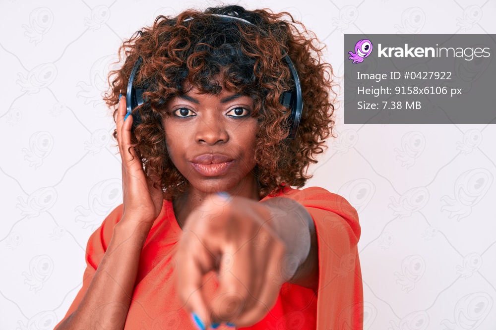 Young african american woman listening to music using headphones pointing with finger to the camera and to you, confident gesture looking serious 