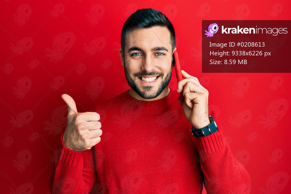 Young hispanic man having conversation talking on the smartphone smiling happy and positive, thumb up doing excellent and approval sign 