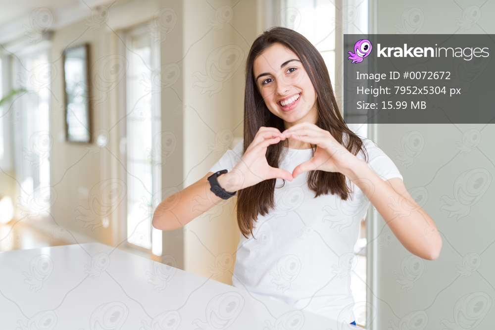 Beautiful young woman wearing casual white t-shirt smiling in love showing heart symbol and shape with hands. Romantic concept.