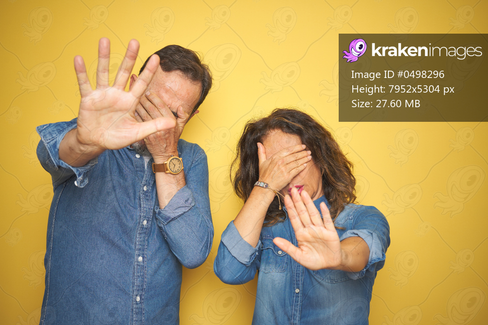 Beautiful middle age couple together standing over isolated yellow background covering eyes with hands and doing stop gesture with sad and fear expression. Embarrassed and negative concept.