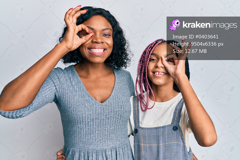 Beautiful african american mother and daughter wearing casual clothes and hugging doing ok gesture with hand smiling, eye looking through fingers with happy face. 