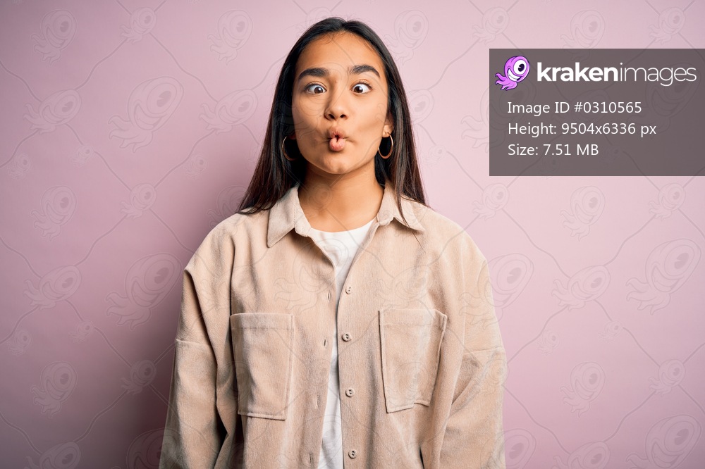 Young beautiful asian woman wearing casual shirt standing over pink background making fish face with lips, crazy and comical gesture. Funny expression.
