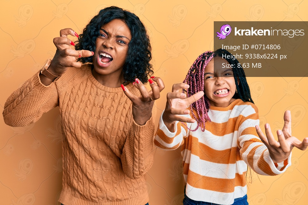 Beautiful african american mother and daughter wearing wool winter sweater shouting frustrated with rage, hands trying to strangle, yelling mad 