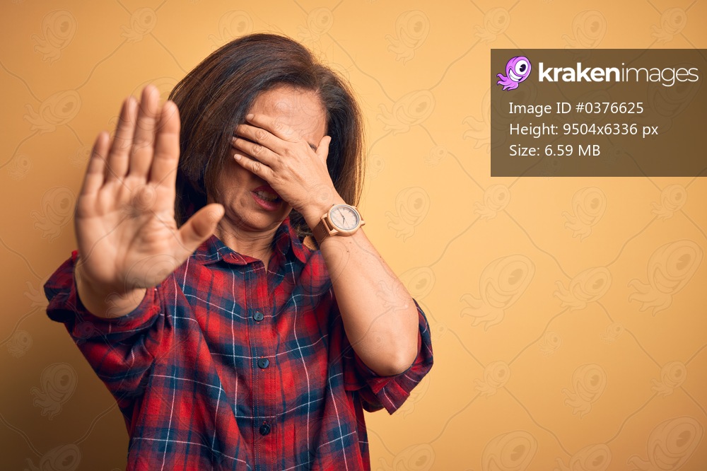 Middle age beautiful woman wearing casual shirt standing over isolated yellow background covering eyes with hands and doing stop gesture with sad and fear expression. Embarrassed and negative concept.