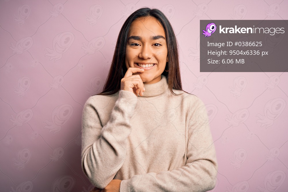 Young beautiful asian woman wearing casual turtleneck sweater over pink background looking confident at the camera with smile with crossed arms and hand raised on chin. Thinking positive.