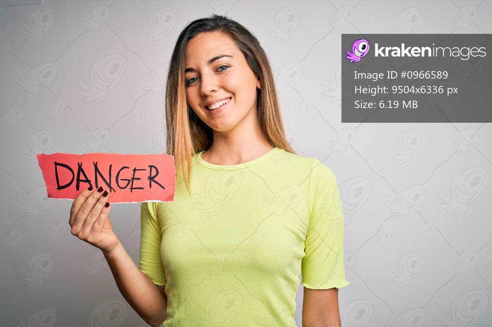 Young beautiful blonde woman with blue eyes holding paper with danger message with a happy face standing and smiling with a confident smile showing teeth