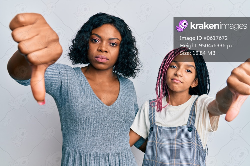 Beautiful african american mother and daughter wearing casual clothes and hugging looking unhappy and angry showing rejection and negative with thumbs down gesture. bad expression. 