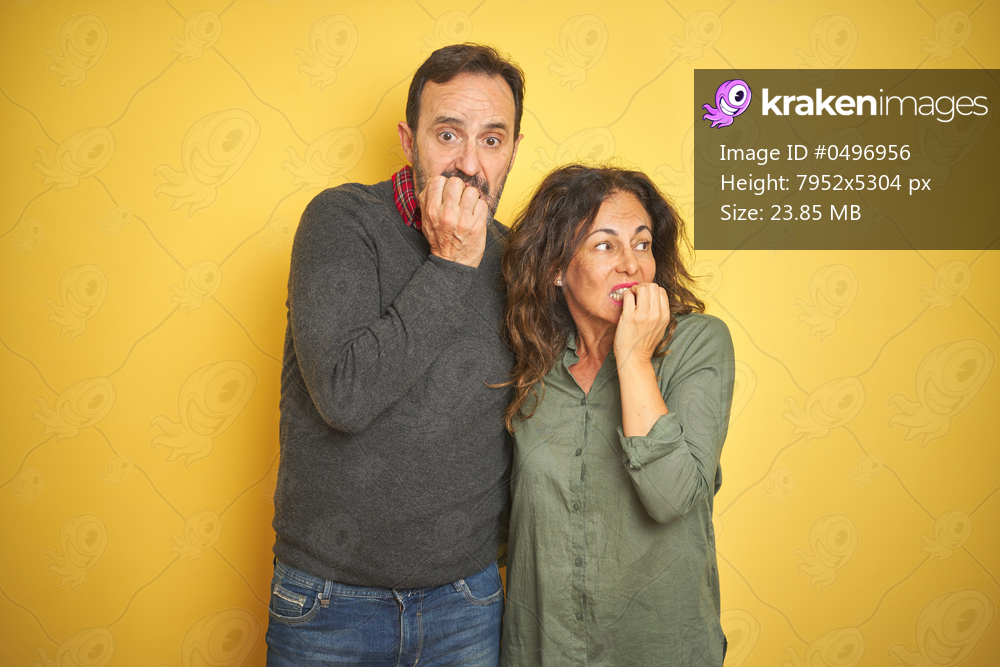 Beautiful middle age couple over isolated yellow background looking stressed and nervous with hands on mouth biting nails. Anxiety problem.