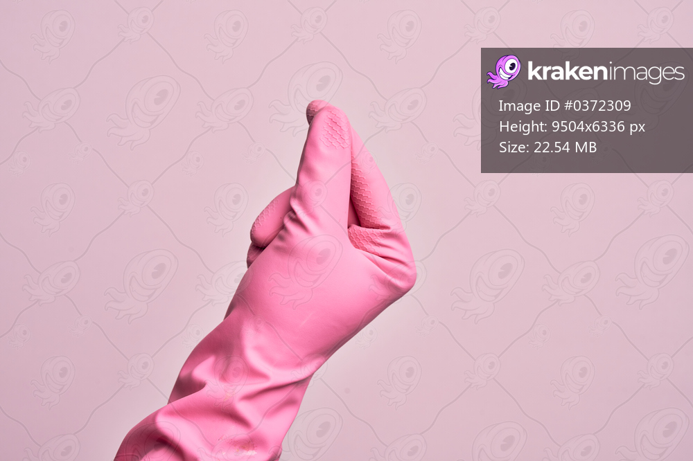 Hand of caucasian young man with cleaning glove over isolated pink background holding blank space with thumb finger, business and advertising