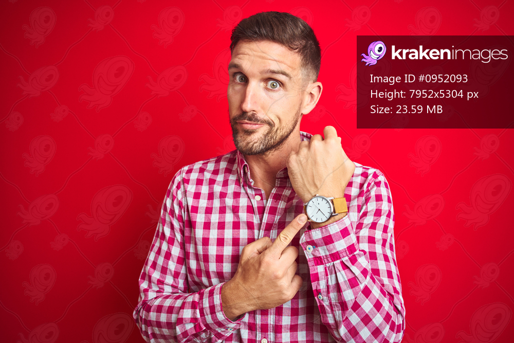 Young handsome man over red isolated background In hurry pointing to watch time, impatience, looking at the camera with relaxed expression