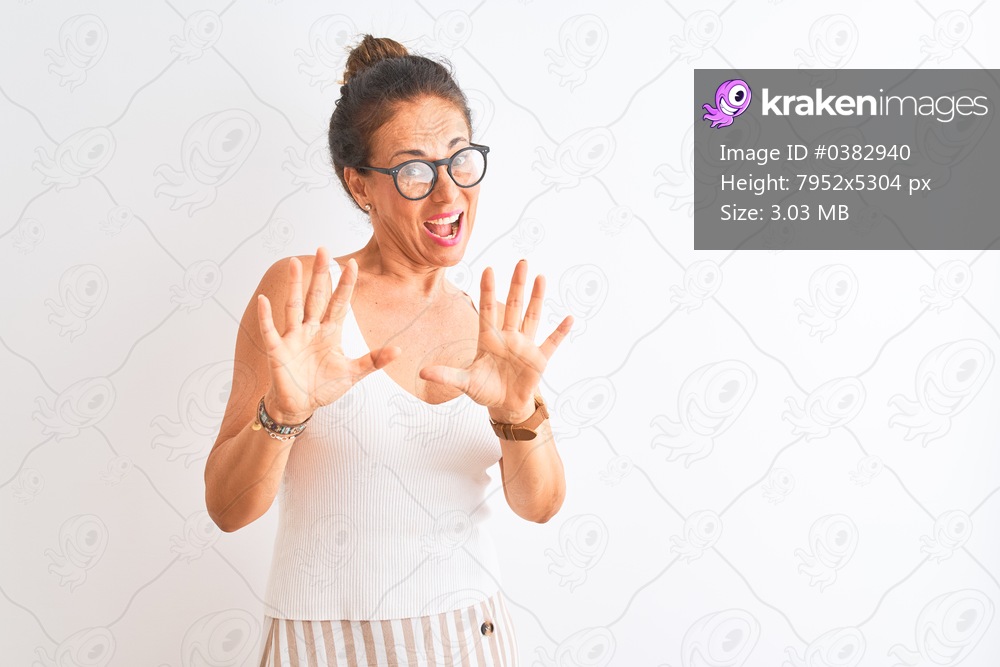 Middle age woman wearing casual t-shirt and glasses standing over isolated white background afraid and terrified with fear expression stop gesture with hands, shouting in shock. Panic concept.