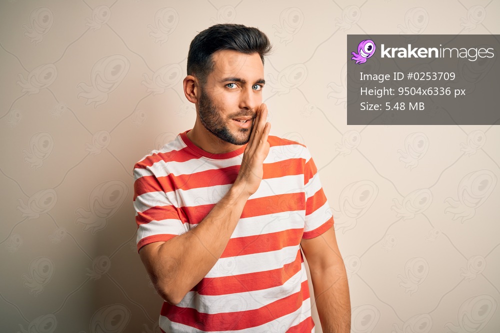 Young handsome man wearing casual striped t-shirt standing over isolated white background hand on mouth telling secret rumor, whispering malicious talk conversation