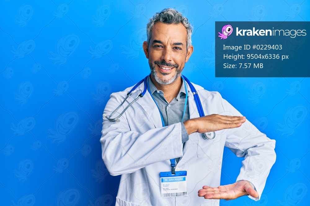 Middle age grey-haired man wearing doctor uniform and stethoscope gesturing with hands showing big and large size sign, measure symbol. smiling looking at the camera. measuring concept. 