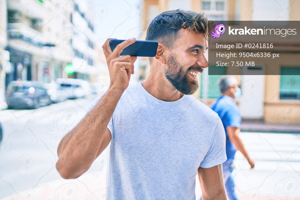 Young hispanic man smiling happy using smartphone walking at the cit