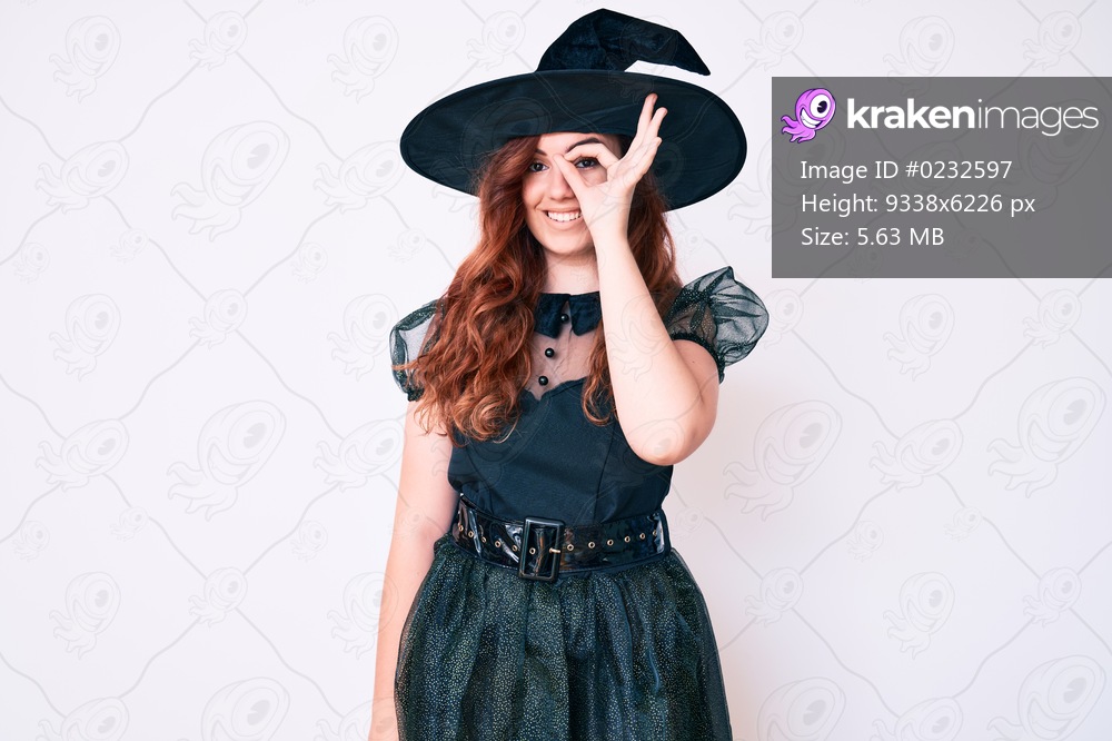 Young beautiful woman wearing witch halloween costume doing ok gesture with hand smiling, eye looking through fingers with happy face. 