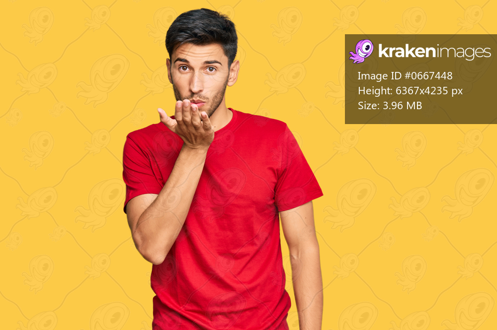 Young handsome man wearing casual red tshirt looking at the camera blowing a kiss with hand on air being lovely and sexy. love expression. 