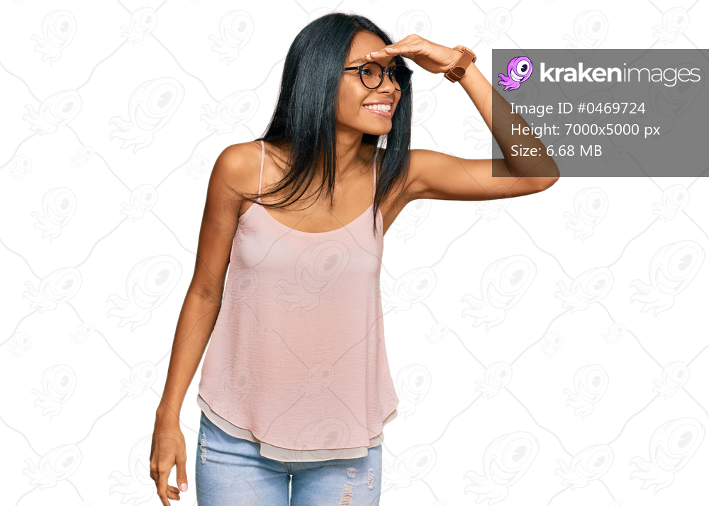 Young african american woman wearing casual clothes and glasses very happy and smiling looking far away with hand over head. searching concept. 