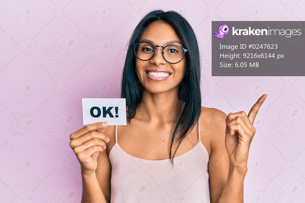 Young african american woman holding ok message paper smiling happy pointing with hand and finger to the side 