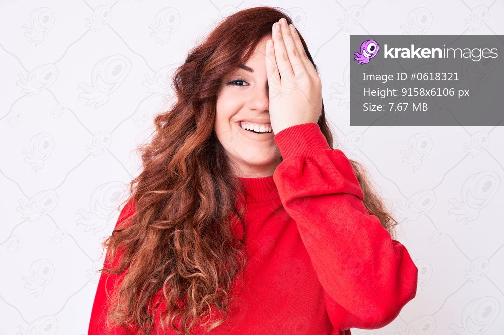 Young beautiful woman wearing casual clothes covering one eye with hand, confident smile on face and surprise emotion. 