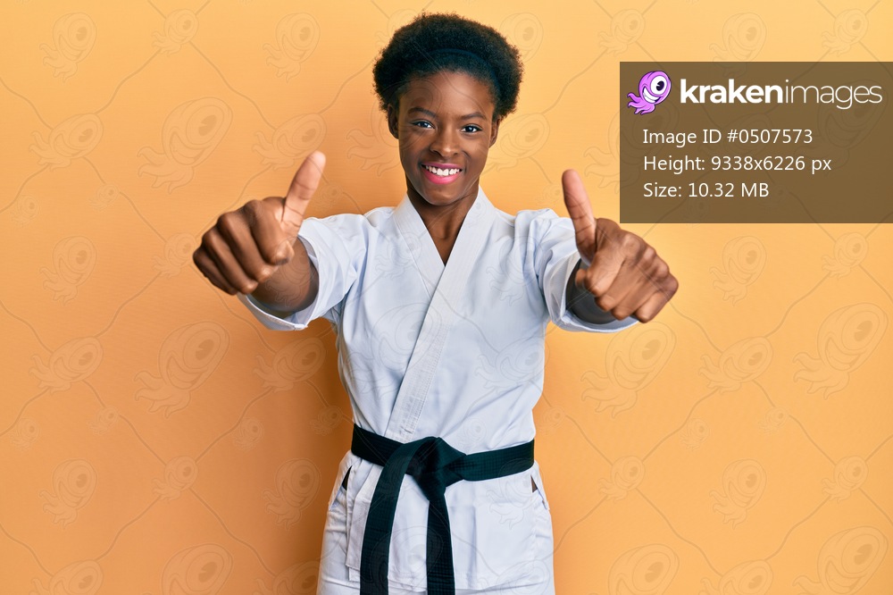 Young african american girl wearing karate kimono and black belt approving doing positive gesture with hand, thumbs up smiling and happy for success. winner gesture. 