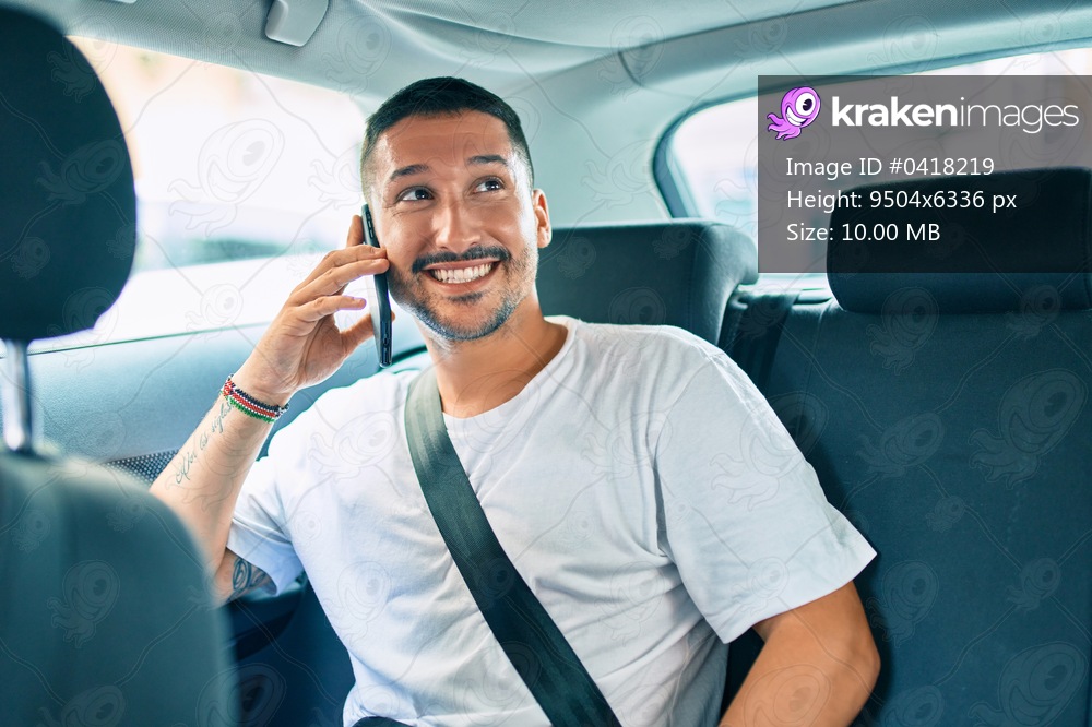 Young hispanic man smiling happy talking on the smartphone sitting on the car.