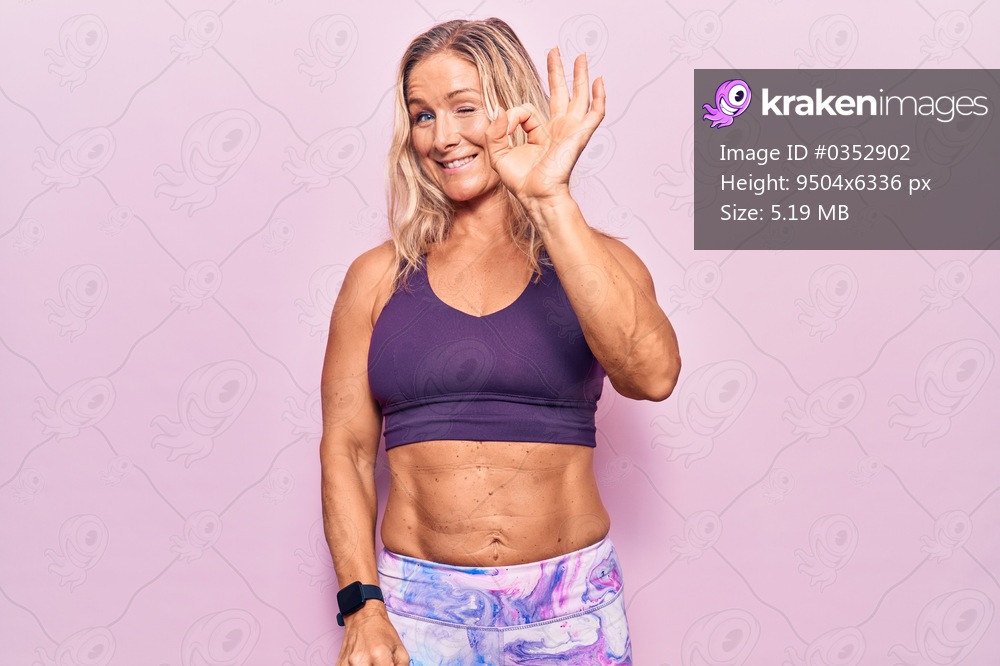 Middle age caucasian blonde woman wearing sportswear over pink background smiling positive doing ok sign with hand and fingers. successful expression. 