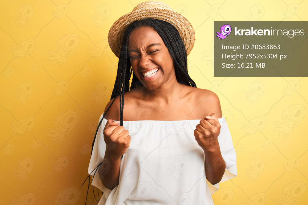 Young african american woman wearing white t-shirt and hat over isolated yellow background very happy and excited doing winner gesture with arms raised, smiling and screaming for success. Celebration concept.