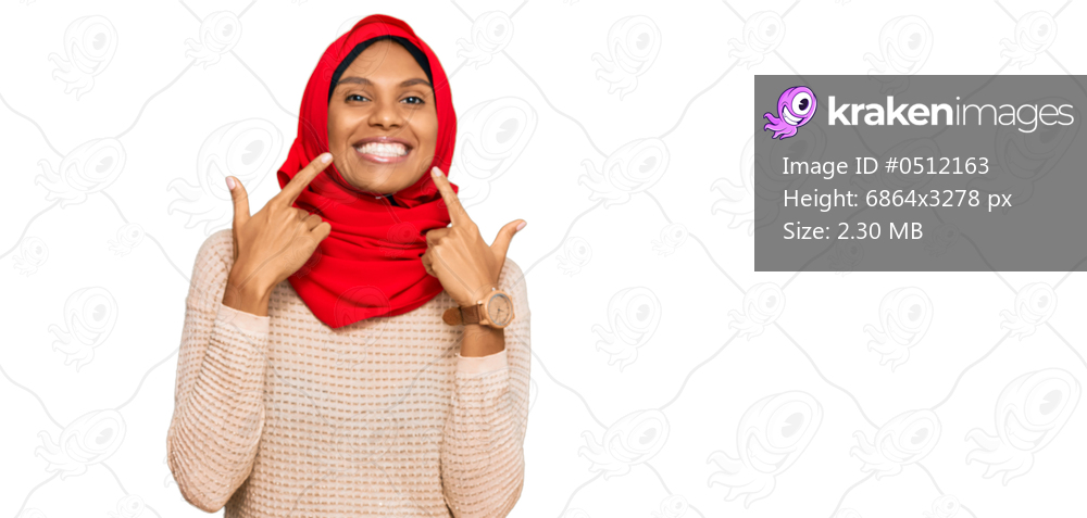 Young african american woman wearing traditional islamic hijab scarf smiling with open mouth, fingers pointing and forcing cheerful smile 