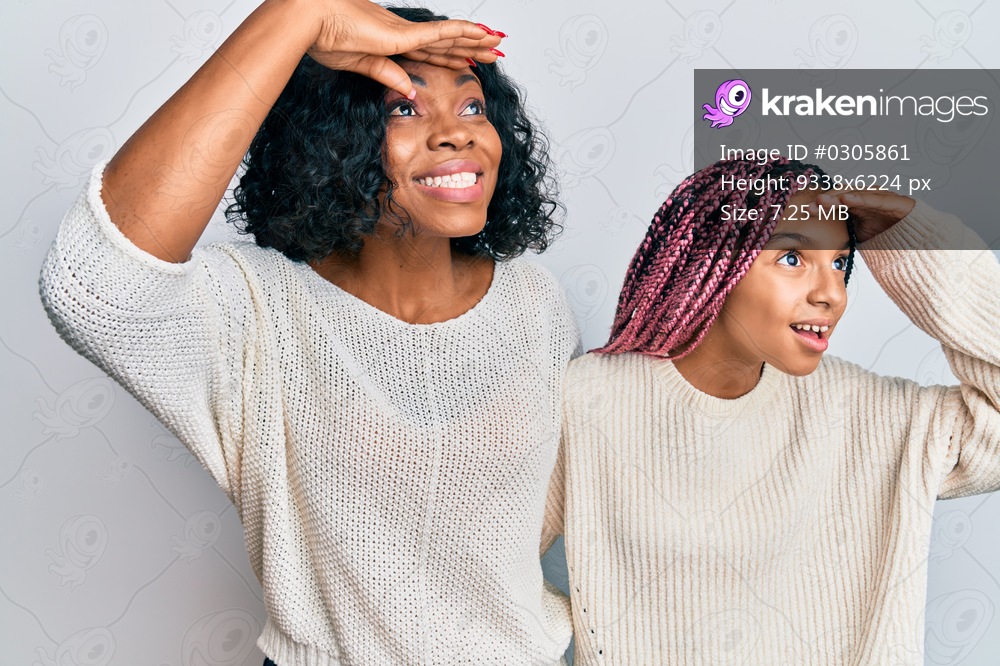 Beautiful african american mother and daughter wearing casual clothes and hugging very happy and smiling looking far away with hand over head. searching concept. 