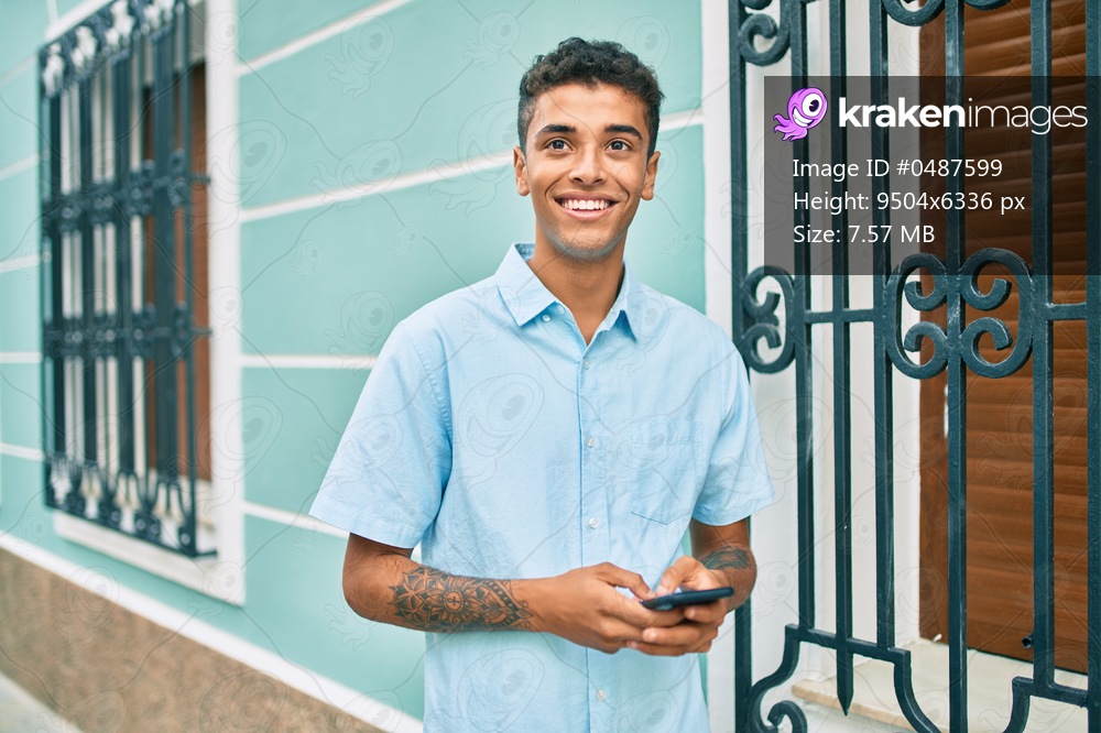Young latin man smiling happy using smartphone walking at the city.