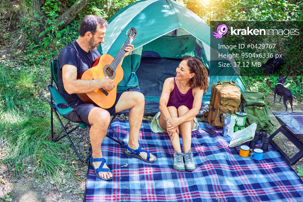 Middle age couple  of hiker smiling happy camping at the forest. Sitting on the floor singing song playing classical guitar