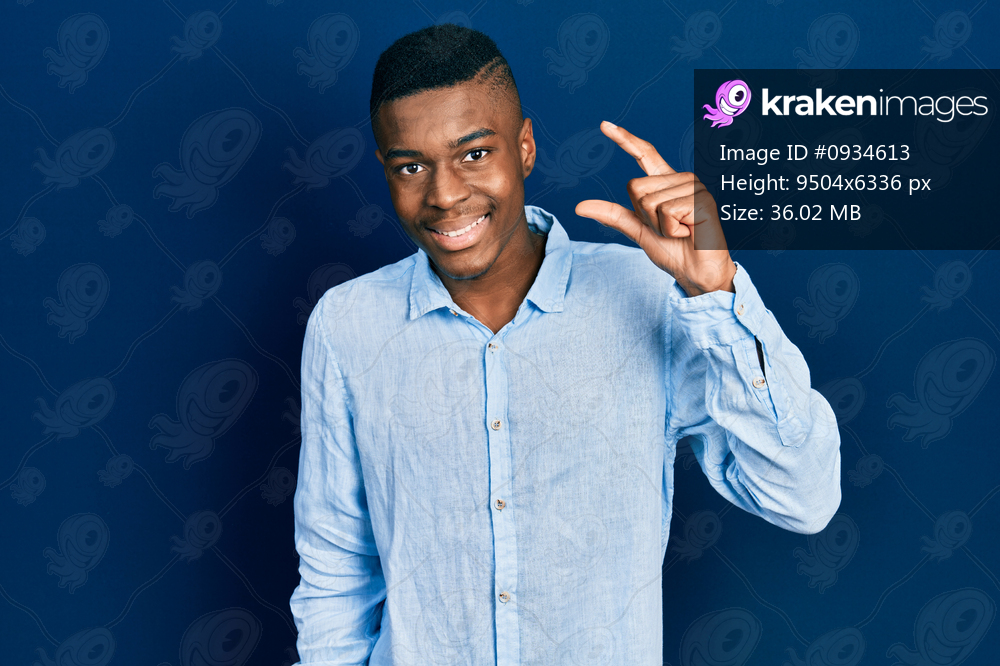 Young african american man wearing casual clothes smiling and confident gesturing with hand doing small size sign with fingers looking and the camera. measure concept. 