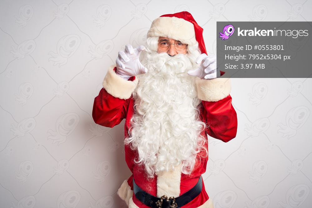 Middle age handsome man wearing Santa costume standing over isolated white background smiling funny doing claw gesture as cat, aggressive and sexy expression