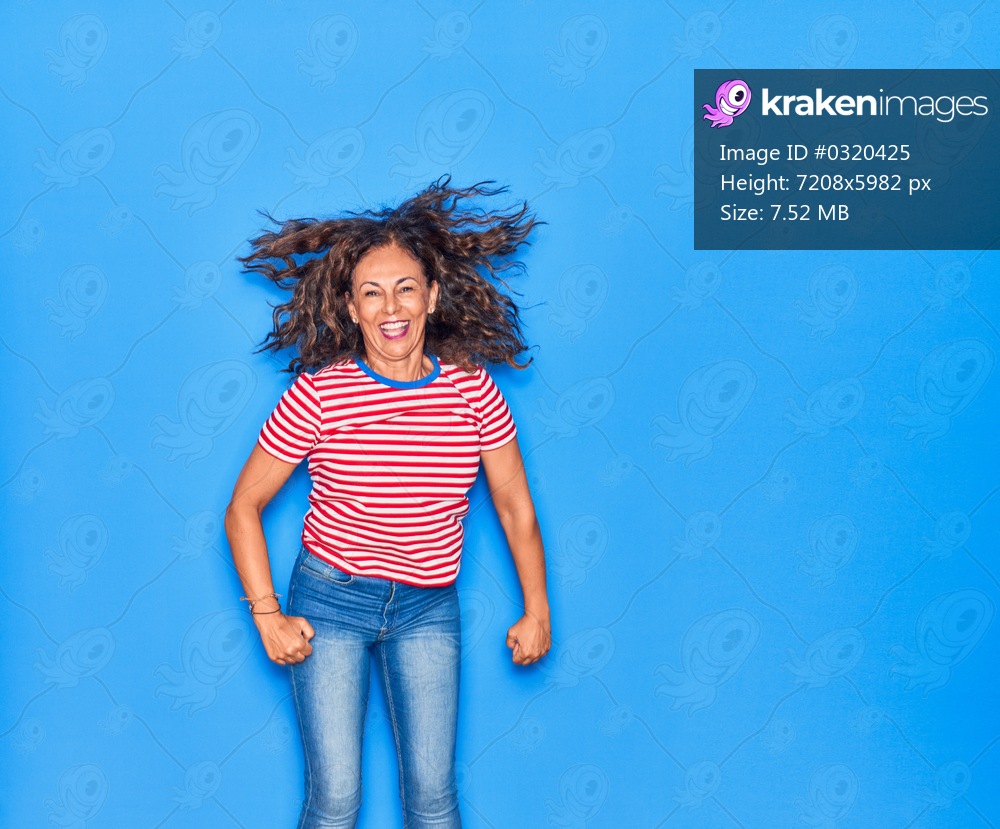 Middle age beautiful hispanic woman wearing casual clothes smiling happy. Jumping with smile on face over isolated blue background
