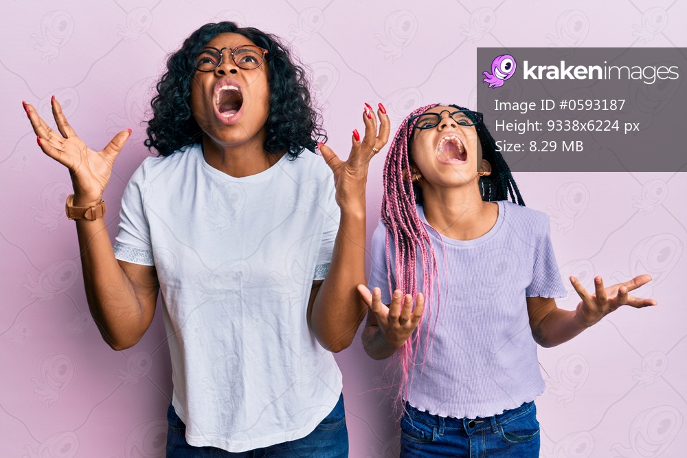 Beautiful african american mother and daughter wearing casual clothes and glasses crazy and mad shouting and yelling with aggressive expression and arms raised. frustration concept. 