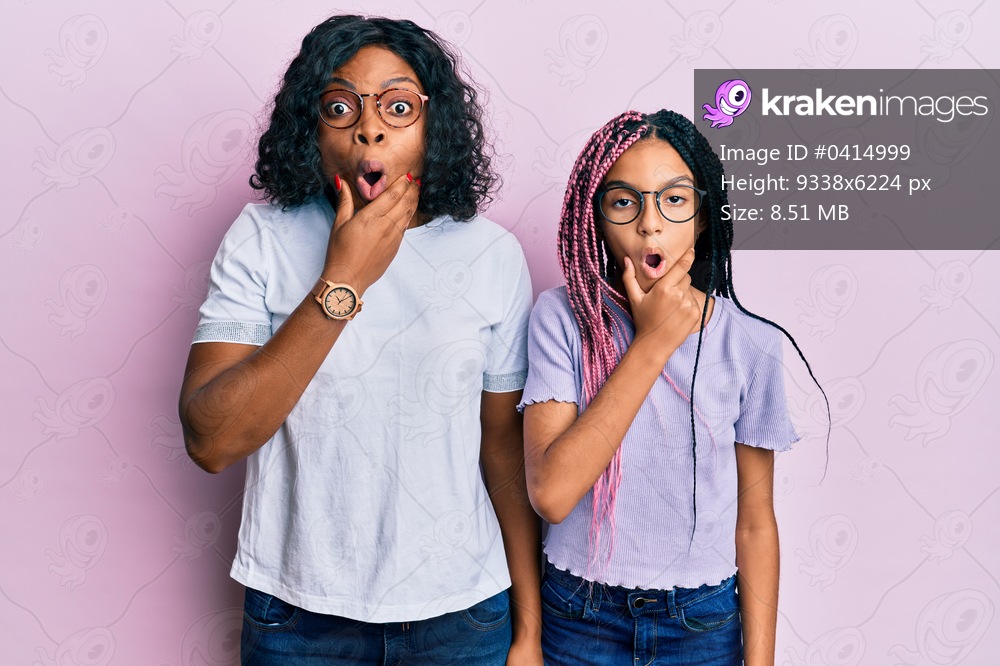 Beautiful african american mother and daughter wearing casual clothes and glasses looking fascinated with disbelief, surprise and amazed expression with hands on chin 