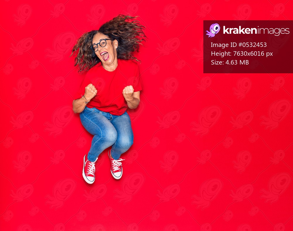 Middle age beautiful hispanic woman wearing casual clothes and glasses smiling happy. Jumping with smile on face over isolated red background