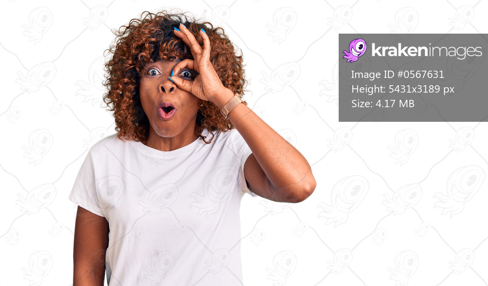 Young african american woman wearing casual white tshirt doing ok gesture shocked with surprised face, eye looking through fingers. unbelieving expression. 