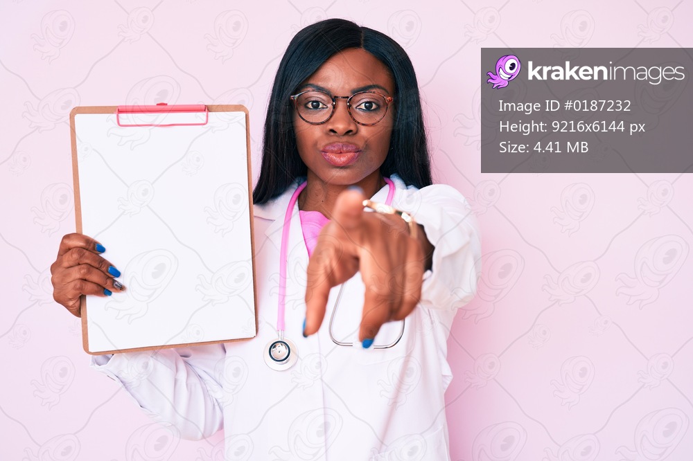 Young african american woman wearing doctor stethoscope holding clipboard pointing with finger to the camera and to you, confident gesture looking serious 
