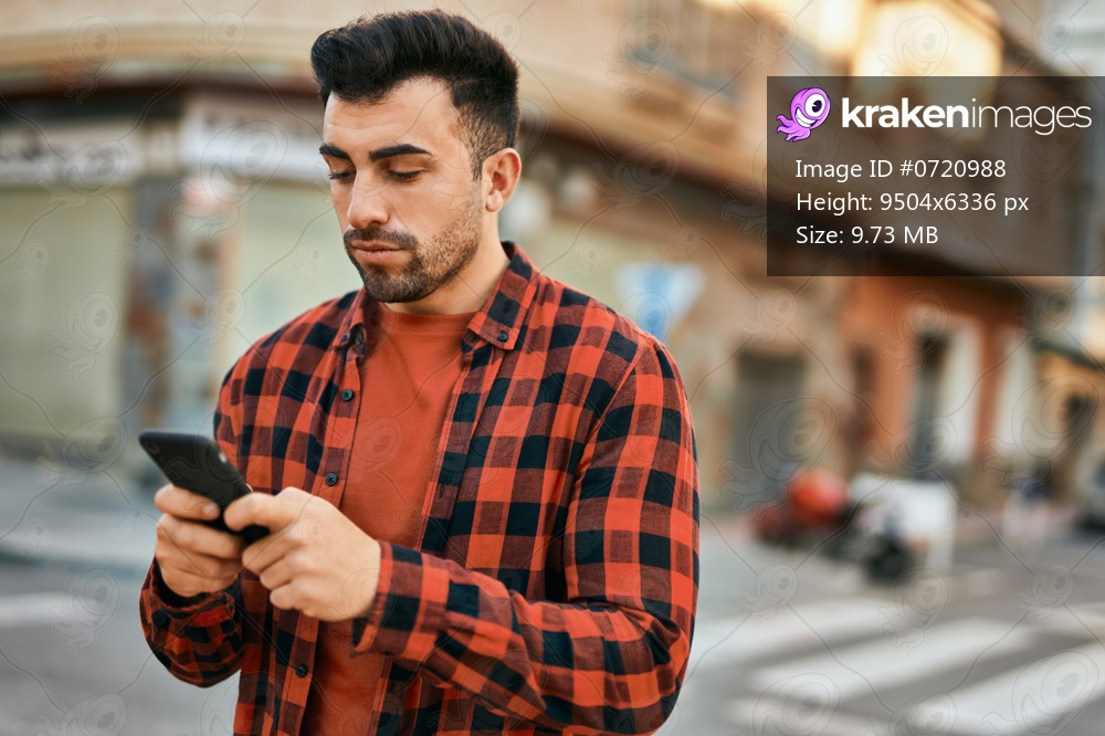 Young hispanic man with serious expression using smartphone at the city.