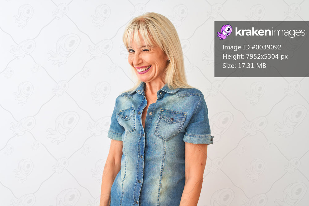 Middle age woman wearing casual denim shirt standing over isolated white background winking looking at the camera with sexy expression, cheerful and happy face.