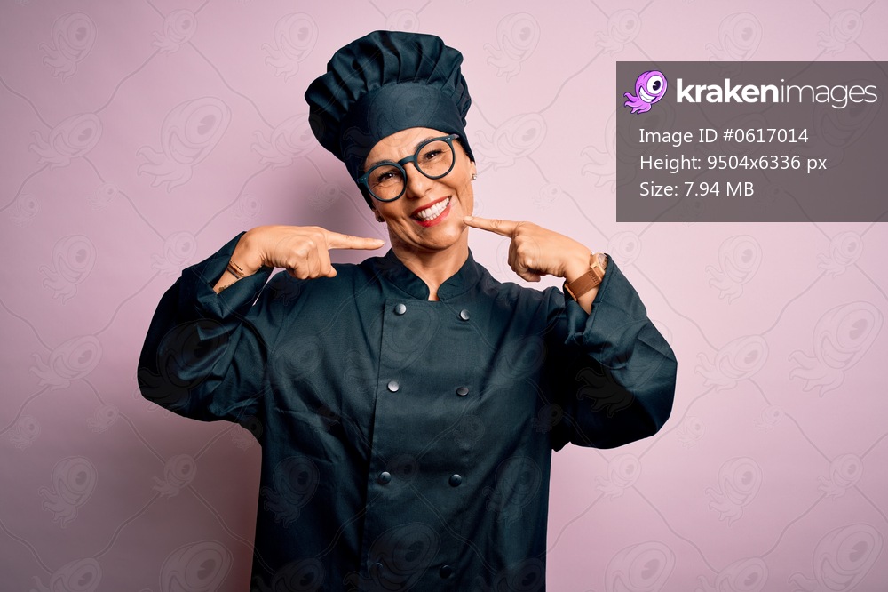 Middle age brunette chef woman wearing cooker uniform and hat over isolated pink background smiling cheerful showing and pointing with fingers teeth and mouth. Dental health concept.